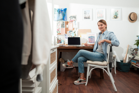 vrouw die thuis aan een bureau zit en in de camera kijkt